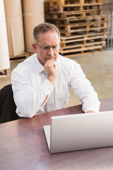 Serious warehouse manager using laptop in a large warehouse