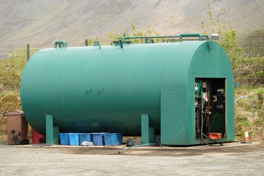 A green fuel storage tank with a pump unit on concrete with waste bins underneath.