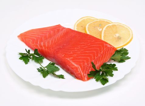 Salmon steak with lemon slices and parsley on white plate