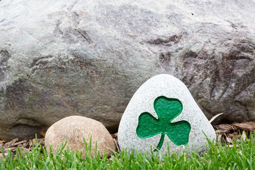 Decorative rock with an incised and painted green shamrock symbolic of Ireland, the Irish, Saint Patrick and the Holy Trinity, standing on green grass with copyspace on the rock behind