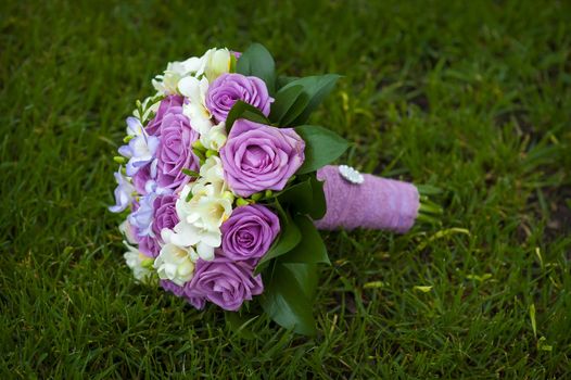 Wedding bouquet of purple and white roses lying on grass.