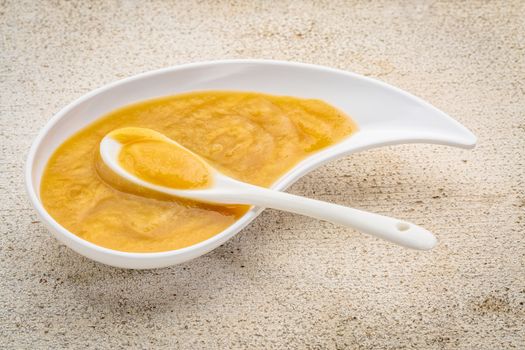 organic fruit and vegetable baby food or snack (apple, corn, sweet potato) - ceramic teardrop shaped bowl with a spoon on a white painted barn wood