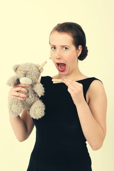 attractive smiling brunette holding teddy bear grimacing with peg on nose in a black dress, retro color