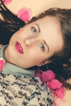 atractive brunette girl lying on beige background, with rose petals around. Beaty concept.