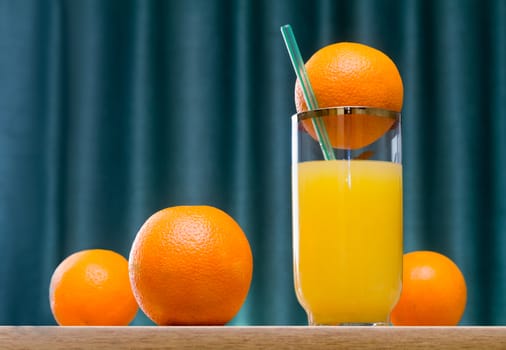 Fresh orange juice in the glass and some oranges on the table..