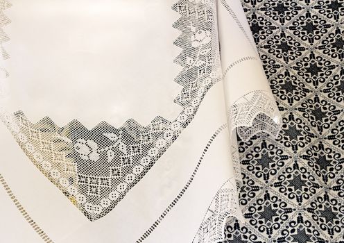 A beautiful white tablecloth, decorated with handmade lace, near bedspread is embroidered with a beautiful pattern of dark blue silk threads.