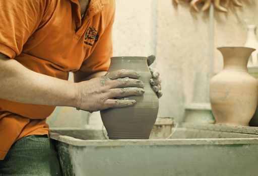 On a rotating pottery wheel wizard manually manufactures ceramic vase.