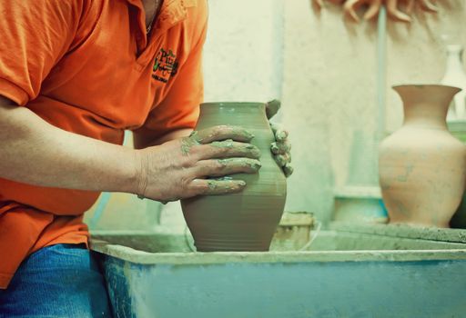 On a rotating pottery wheel wizard manually manufactures ceramic vase.