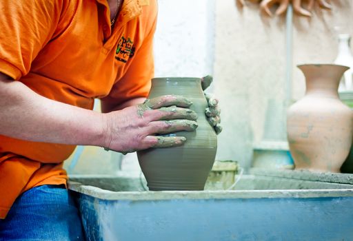 On a rotating pottery wheel wizard manually manufactures ceramic vase.