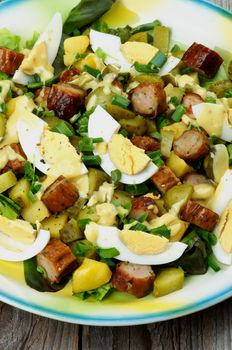 Delicious Potato and Sausage Salad with Gherkins, Lettuce, Boiled Eggs and Mustard Sauce closeup on Yellow and Blue Plate