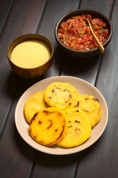 Plate of arepas with Colombian hogao sauce (tomato and onion cooked) and corn meal in the back. Arepas are made of yellow or white corn meal and are traditionally eaten in Colombia and Venezuela (Selective Focus, Focus on the first arepas)