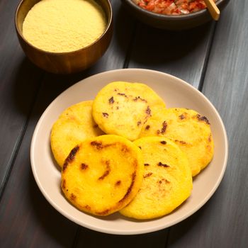 Plate of arepas with Colombian hogao sauce (tomato and onion cooked) and corn meal in the back. Arepas are made of yellow or white corn meal and are traditionally eaten in Colombia and Venezuela (Selective Focus, Focus on the first arepas)