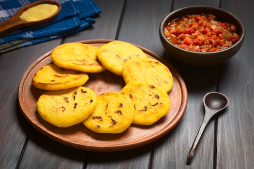 Wooden plate of arepas with Colombian hogao sauce (tomato and onion cooked) in the back. Arepas are made of yellow or white corn meal and are traditionally eaten in Colombia and Venezuela (Selective Focus, Focus on the first arepas)