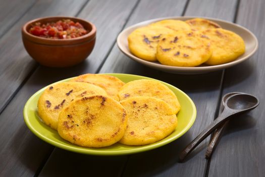 Two plates of arepas with Colombian hogao sauce (tomato and onion cooked) in the back. Arepas are made of yellow or white corn meal and are traditionally eaten in Colombia and Venezuela (Selective Focus, Focus on the first arepas)