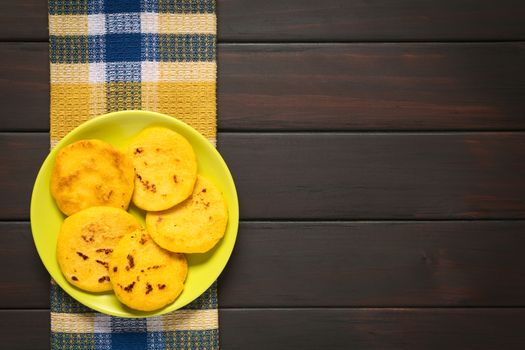 Plate of arepas photographed on dark wood with natural light. Arepas are made of white or yellow corn meal (here yellow) and are traditionally eaten for breakfast or as snack in Colombia and Venezuela.