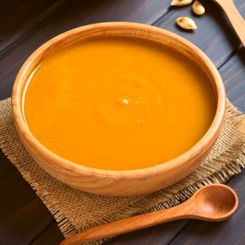 Cream of pumpkin soup served in wooden bowl, photographed on dark wood with natural light (Selective Focus, Focus on the middle of the soup) 