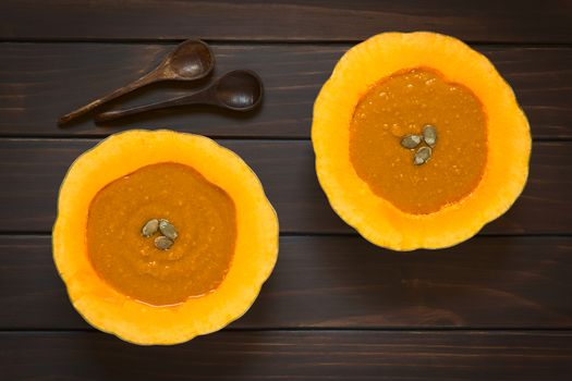 Cream of pumpkin soup served in half pumpkins with pepita seeds on top, photographed overhead on dark wood with natural light