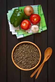 Raw textured vegetable or soy protein, called also soy meat in wooden bowl with raw vegetables on kitchen towel. Photographed overhead on dark wood with natural light. 
