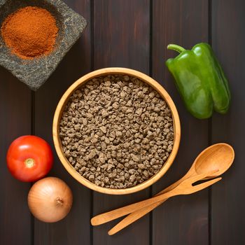 Raw textured vegetable or soy protein, called also soy meat in wooden bowl with raw vegetables and paprika in mortar. Photographed overhead on dark wood with natural light. 