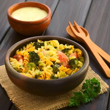 Baked tricolor fusilli pasta and vegetable (broccoli, tomato) casserole in rustic bowl, wooden cutlery on the side, cream sauce in the back, photographed with natural light (Selective Focus, Focus in the middle of the dish)