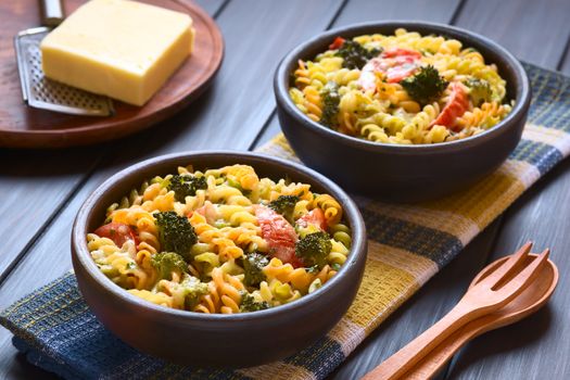 Baked tricolor fusilli pasta and vegetable (broccoli, tomato) casserole in rustic bowls, wooden cutlery on the side, grater and cheese in the back, photographed with natural light (Selective Focus, Focus in the middle of the first dish)
