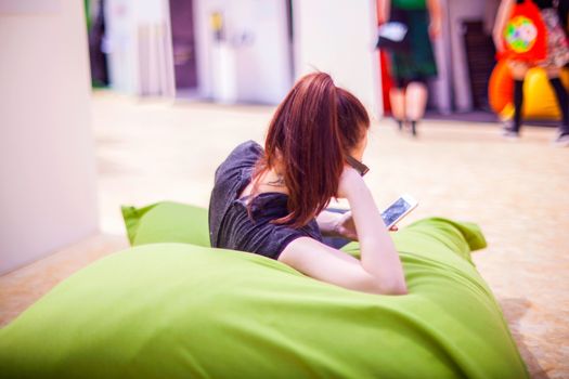 MILAN, ITALY - APRIL 16: Pretty woman reading message on smartphone while sitting on green pouf during Milan Design week on April 16, 2015