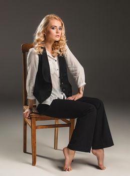 Beauty blond woman  in a black suit and white shirt, sitting on a chair on a gray background