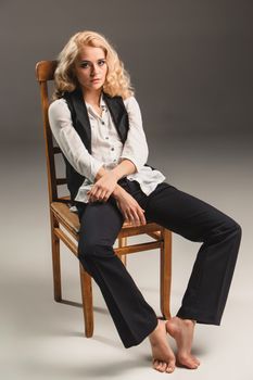 Beauty blond woman  in a black suit and white shirt, sitting on a chair on a gray background