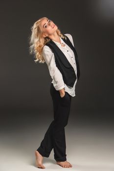 Beauty blond woman  in a black suit and white shirt on a gray background. Portrait in full growth