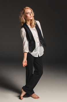 Beauty blond woman  in a black suit and white shirt on a gray background. Portrait in full growth