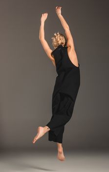 Beauty blond woman  in a black coveralls on a gray background. Portrait in full growth. view from the back