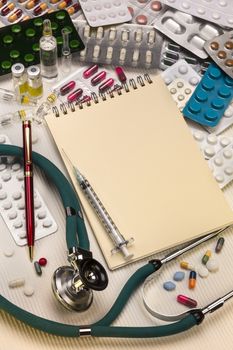 A doctors stethoscope and drugs with syringes and a notepad and pen - with space for text.