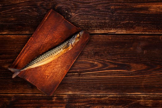 Smoked mackerel on wooden chopping board, on old vintage textured wooden table, top view. Vintage style fish with copy space.