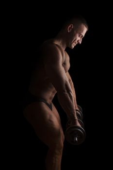 Sexy shirtless bodybuilder lifting weights isolated on black background. Extreme strength, muscles and fitness.