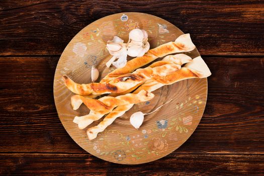 Pizza bread with garlic on wooden plate on brown vintage wooden table, top view. Culinary pizzastick eating, rustic styles.