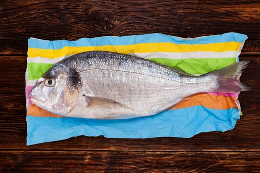 Fresh sea bream fish on colorful napkin on vintage wooden table. Culinary seafood eating.