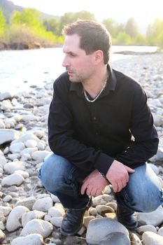 Attractive brunette male sitting on a pebble beach