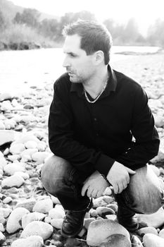 Attractive brunette male sitting on a pebble beach