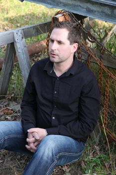 Attractive brunette male sitting outdoors in a field with ruins