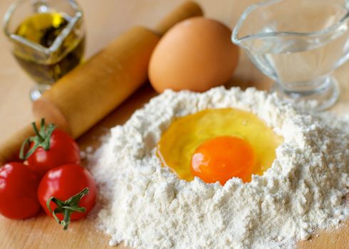 Preparing Pasta Dough. Ingredients with Flour, Olive Oil, Egg, Water and Wooden Rolling Pin closeup on Wooden Kitchen Table