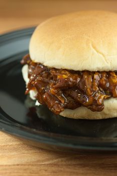A barbecue pork sandwich on a black plate on a wooden counter top.