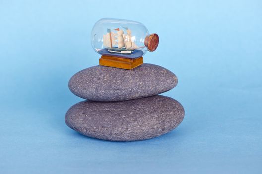 small ship sailboat model in glass bottle on sea stone and azure background