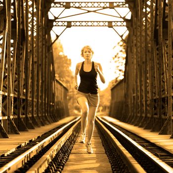 Athlete running on railaway tracks bridge in morning sunrise training for marathon and fitness. Healthy sporty caucasian woman exercising in urban environment. Active urban lifestyle.