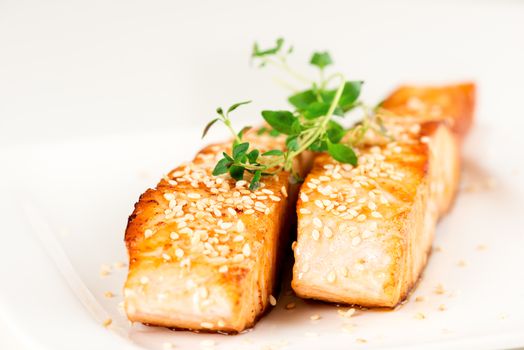 Grilled salmon, sesame seeds  and marjoram on white plate. Studio shot