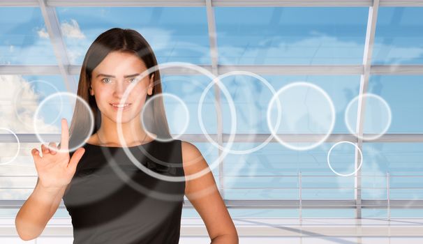 Young businesswoman in dress pressing on holographic screen with circles and looking at camera