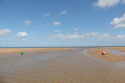 A view down a low tide marine channel with a green, can buoy, and a red, nun buoy, day markers looking out to the open sea.