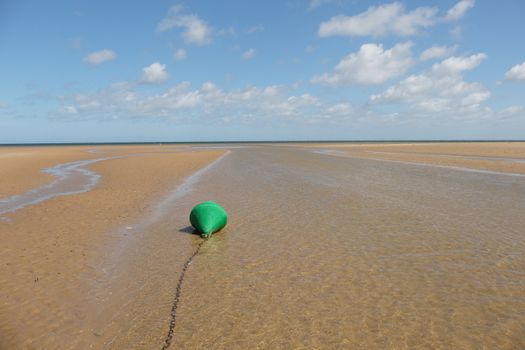 A chained channel day marker, green, can buoy, at low water looking out to sea,