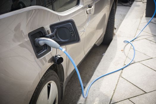 Charging an electric car at a roadside urban charging station showing a close up of the attached connector and cable in a green energy concept