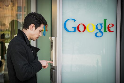 Handsome young man standing ringing the intercom at Google offices