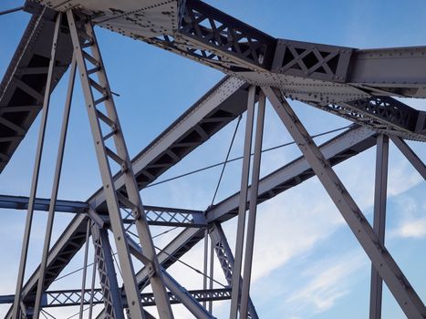 Detail shot of an historic gray painted Dutch riveted truss bridge against a blue sky.